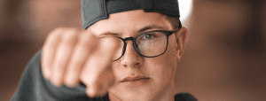 young person in glasses and backward baseball hat pointing directly at the camera