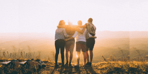 group of four people with their harms around each other at sunset