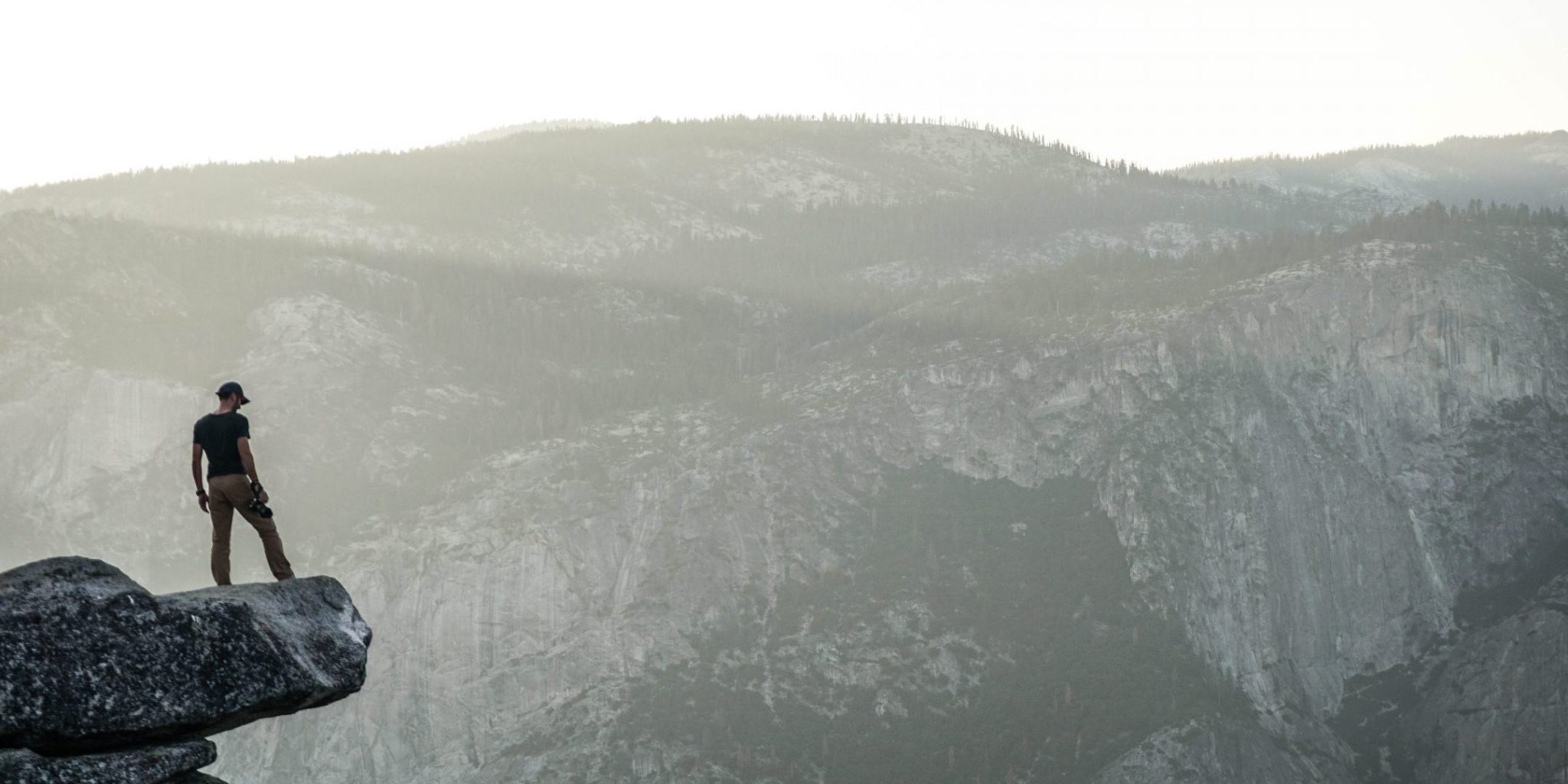 person standing on a overhanging rock in the mountains