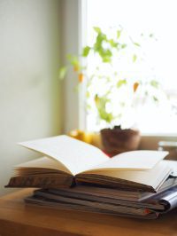 Open book with blank pages stacked on another book with a window and plant behind it