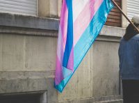 a transgender pride flag in front of a gray building